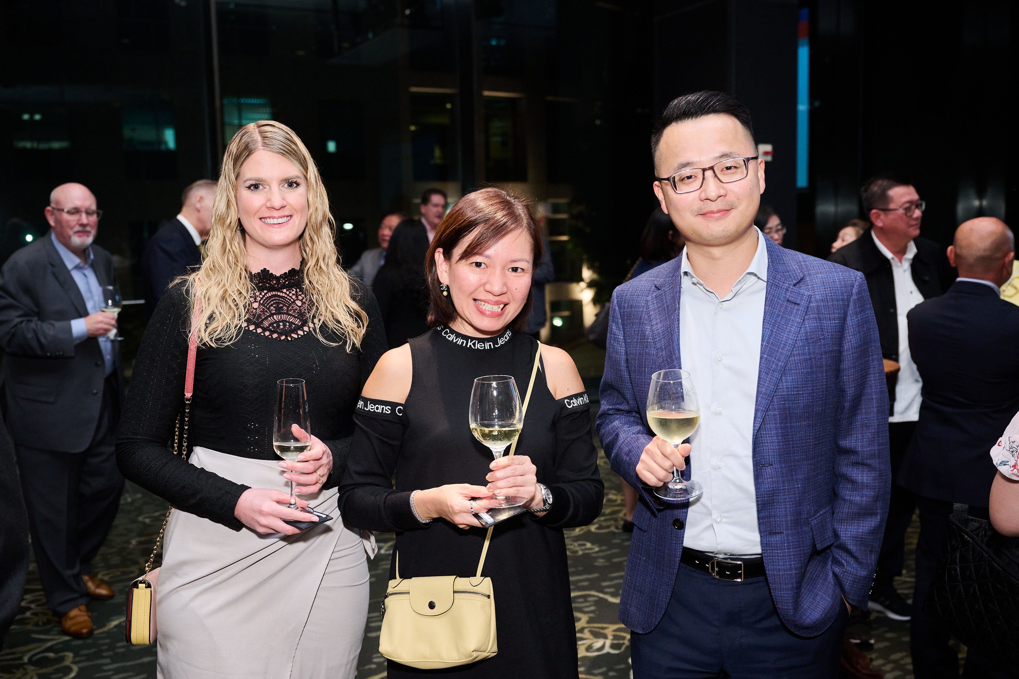 A woman with blonde hair, a woman with brown hair in a bob and a man wearing glasses smile at the camera.
